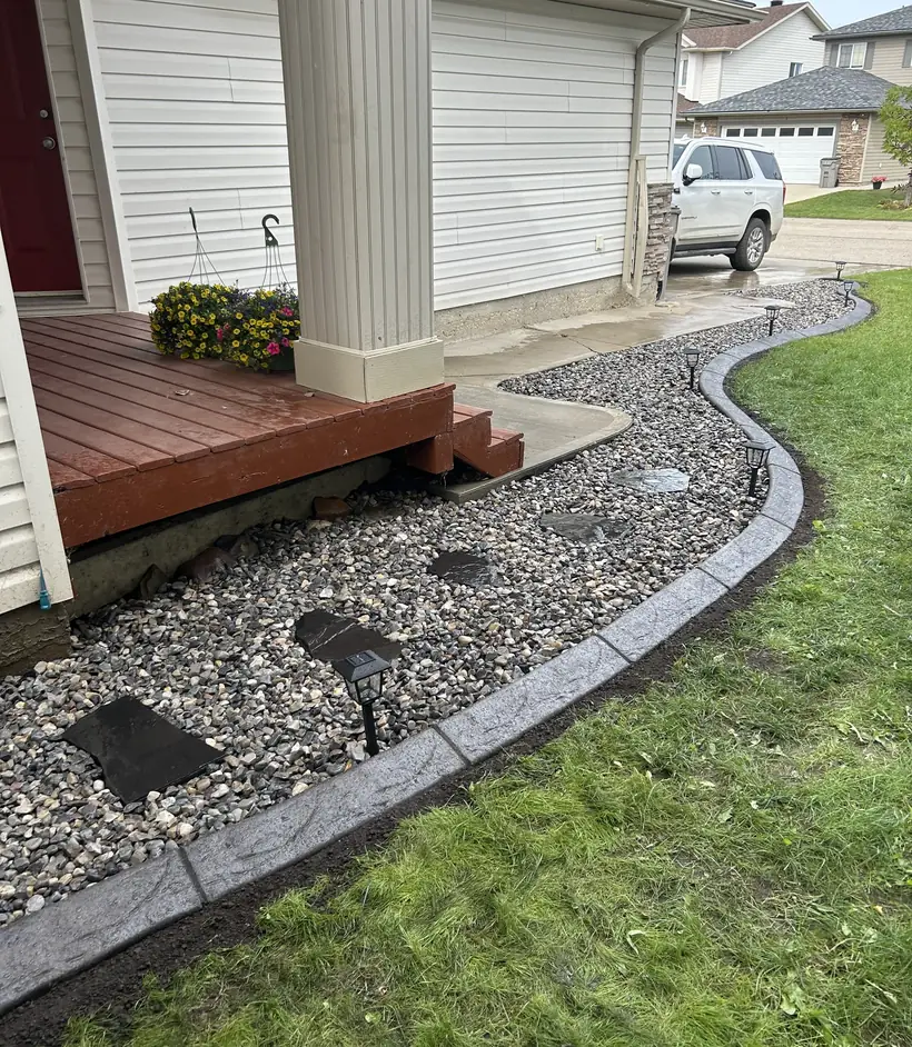 Concrete curbing and decorative rock bed running along the side of a house
